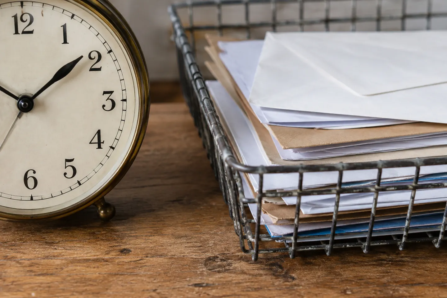 Close-up of an analogue clock and a stack of sorted correspondence in a wire tray