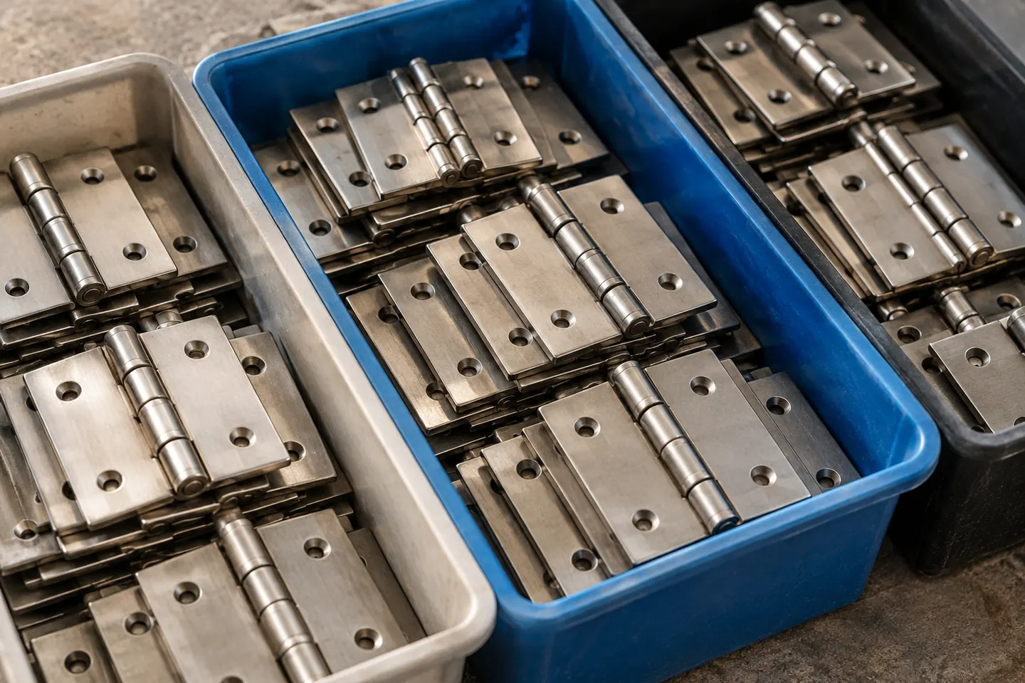 Three unlabeled parts bins containing identical steel hinges, matching shapes arranged neatly for comparison, side light macro